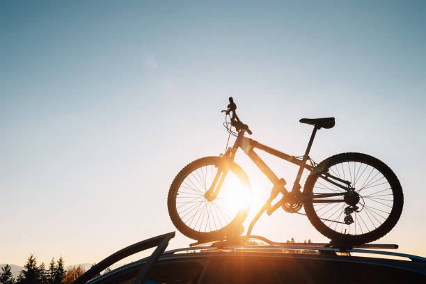 istock Mounted mountain bicycle silhouette on the car roof with evening sun light rays background. Safe sport items transportation using a car concept image. 1176312628
