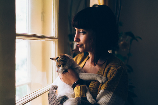 Woman hugging cat and looking through the window