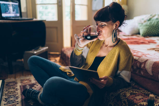 Home sweet home Young woman at home drinking red wine and using tablet e reader photos stock pictures, royalty-free photos & images