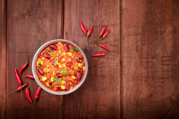 chili con carne, a mexican stew with red beans, meat, and chili peppers, shot from the top on a dark rustic wooden background with a place for text - vegetable pepper food chili pepper imagens e fotografias de stock