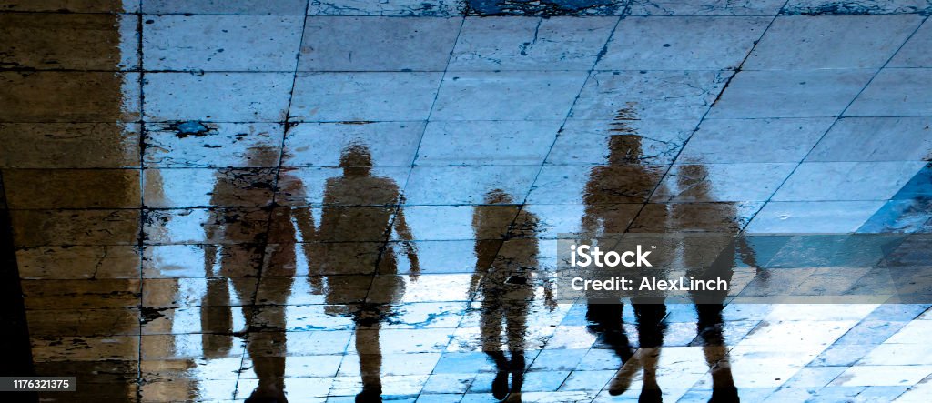 Reflection shadow silhouette on wet city sidewalk of mysterious people walking away the night Blurry reflection shadow silhouette on wet city sidewalk of mysterious people walking away the night, low angle view In Silhouette Stock Photo