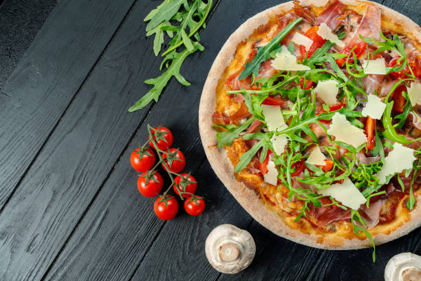 Homemade fresh Pizza with jamon, arugula, parmesan and cherry tomatoes on a black wooden with copy space. Top view food photo. Flat lay. Italian cuisine. stock photo
