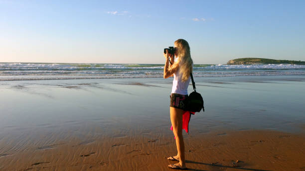 istock Blonde girl with camera shooting on the beach 1176329809