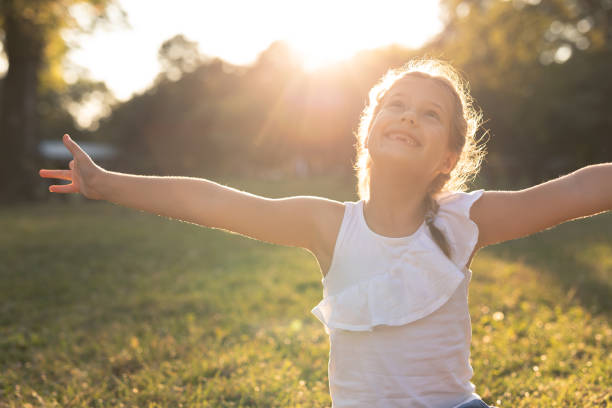 Portrait of a happy child enjoying summer day in the park. Happy girl sitting on the grass and smiling