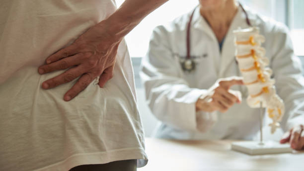 A doctor explaining lumbar anatomy to back pain patient A male doctor explaining lumbar anatomy to female patient complaining of back pain at medical clinic low section stock pictures, royalty-free photos & images