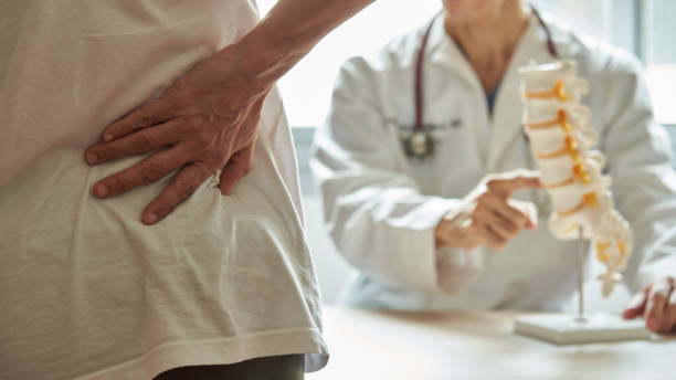 A doctor explaining lumbar anatomy to back pain patient A male doctor explaining lumbar anatomy to female patient complaining of back pain at medical clinic spinous process stock pictures, royalty-free photos & images