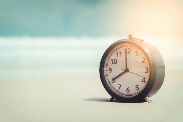 istock Clock on sand beach in morning suns light with smooth wave background. Copy space of time and summer holiday concept. 1176334763