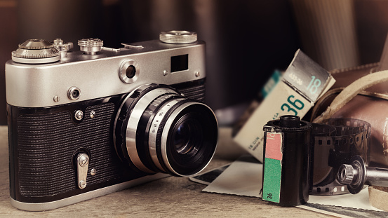Old retro camera, cassette, photo film roll and photos on wooden table. Vintage stylized image.