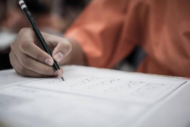 istock Exam test school or university concept : Hand student holding pencil writing standardized answer multiple carbon paper form with gray black answers sheet bubbled doing final assessment in classroom 1176339265