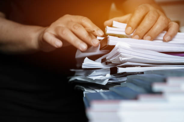 istock Business documents paperwork overwork concept : Employee people hands working in stacks paper files for searching and checking unfinished document report on folders print at busy work desk office. 1176339482
