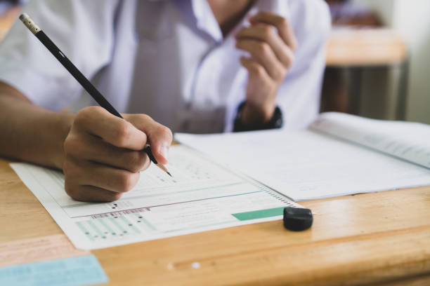 istock School / university Students hands taking exams, writing examination room with holding pencil on optical form answers paper sheet on desk doing final test in classroom. Education assessment Concept 1176339517