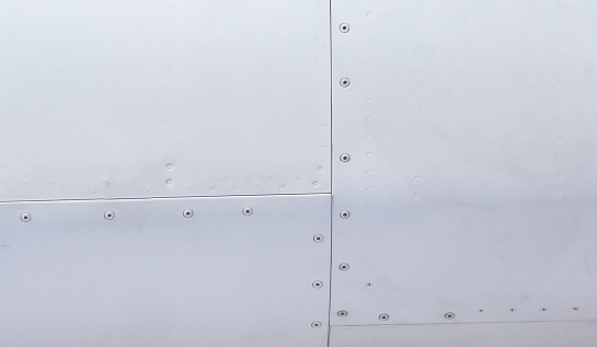 Silver metal surface of the aircraft fuselage with rivets. Fuselage detail view. Airplane metallic fuselage detail with rivets.