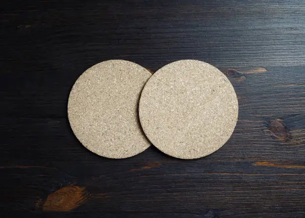 Two blank cork beer coasters on wood table background. Flat lay.