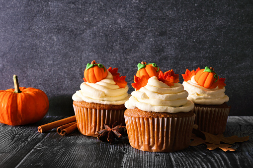 Fall pumpkin spice cupcakes with creamy frosting and autumn toppings. Side view scene against a dark background.