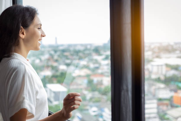 Beautiful woman look at nice view of cityscape at condominium room or hotel of hig building. Gorgeous woman wear bathrobe. Pretty girl get fresh, happiness with smiley face. Glamour lady feel relaxing hermosa mujer mira a la bonita vista del paisaje urbano en la habitación del condominio o el hotel del edificio de hig. hermosa mujer usar albornoz. chica bonita conseguir fresco, felicidad con la cara sonriente. glamour dama se siente relajante