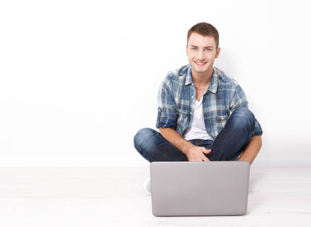 istock Satisfied with work done. Happy young man working on laptop while sitting on the floor near the wall at home. 1176371001