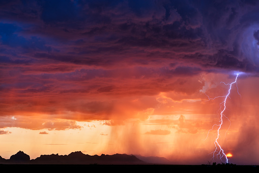 A lightning bolt strikes next to the setting sun as a thunderstorm moves through the desert near Salome, Arizona.