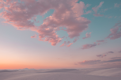 Pink cotton candy clouds stretch across the sky over the white sand dunes at sunset in White Sands National Monument, New Mexico, USA.
