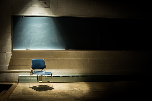Una silla escolar vacía en un aula oscura y sombría - frente a una pizarra con un solo haz de luz en la cabeza photo