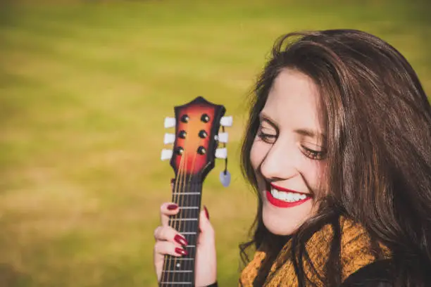 Vivacious happy young woman with a guitar enjoying the autumn sunshine in a park in a close up on her face and lovely warm smile with copy space on grass