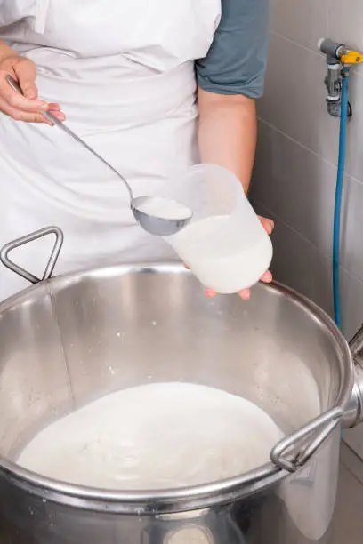 Cheesemaker pours the rennet with a ladle and a jug