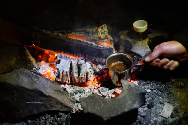 Boiling coffee in turkish cezva on campfire coals. Luxury camping concept.