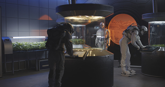 Medium shot of astronauts and humanoid robot examining plant incubators on a Mars base