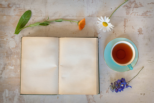 Blank page open book with copy space, flowers and cup of tea on the table.