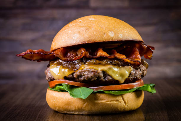 istock Craft beef burger with cheese, bacon, caramelized onion and rocket leafs on wood table and rustic background 1176404221