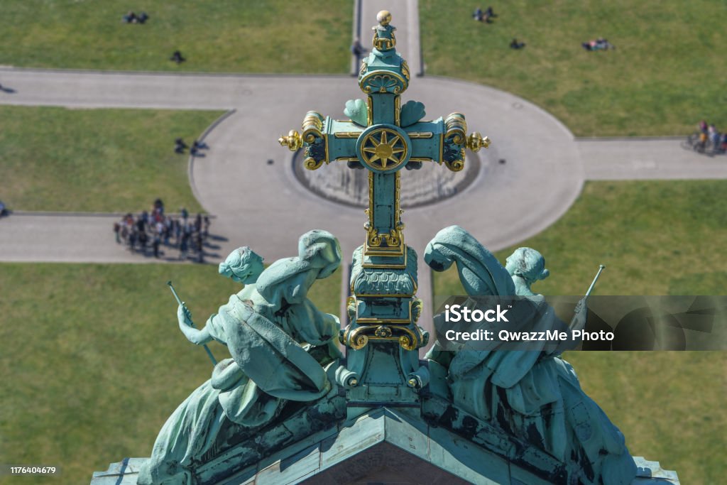 Cross overseen the world In focus cross on the top of Berliner Dom. On the background, a grass lawn with sparse people around it including a group of tourists. Berlin Cathedral Stock Photo