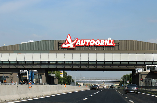 Milan, Italy - June 15, 2019: Highway on the way to Milan with cars on both sides of freeway and Autogrill restaurant with logo across on overlay bridge.