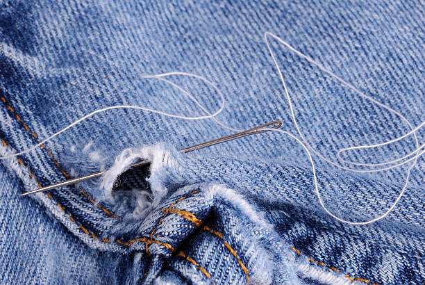 A needle and thread with a pair of jeans needing mending.