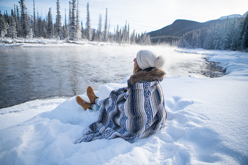 One girl relaxing in winter by the river contemplating nature under a blanket