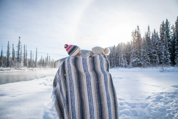 istock Couple sitting in snow by the river wrapped in blanket 1176410138