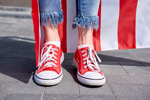 Woman's legs in stylish jeans and trendy red sneakers. American flag on background.