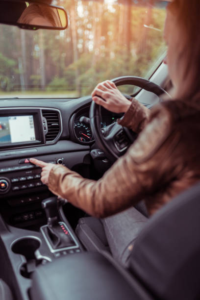 Girl woman in car interior leather jacket autumn and spring, in forest park, presses emergency stop button, switches on dimensions, accident on road, obstacle to cars signal about the accident. stock photo