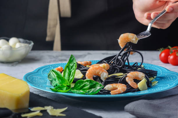 istock Fancy spaghetti with shrimp, parmesan and basil. Girl's hands wind black pasta with cuttlefish ink on a fork. Tasty dinner. 1176416347