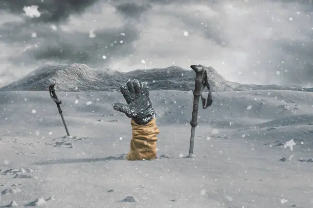 Hiker stretching out his snow covered hand next to trekking poles to signal help because of snow avalanche . Danger extreme concept