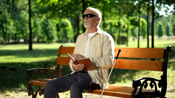 istock Blind pensioner reading braille book, sitting on bench in summer park, resting 1176425507
