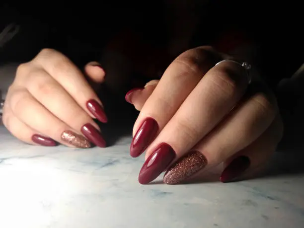 Long nails coated with red-wine color. Burgundy gel polish on long nails with sequins design