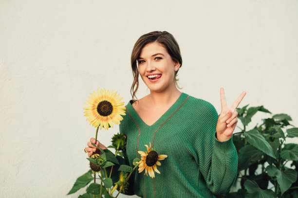 Photo of Outdoor portrait of beautiful young woman wearing warm green knitted pullover, posing with sunflower