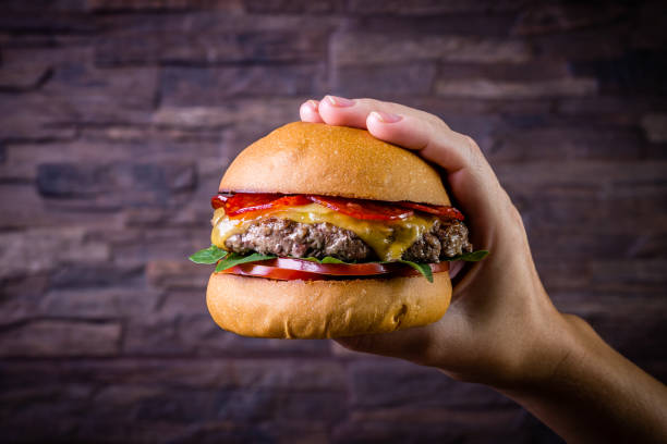 istock Hand holding a craft beef burger with cheese, italian peperoni, tomato and basil leafs on rustic background 1176437447