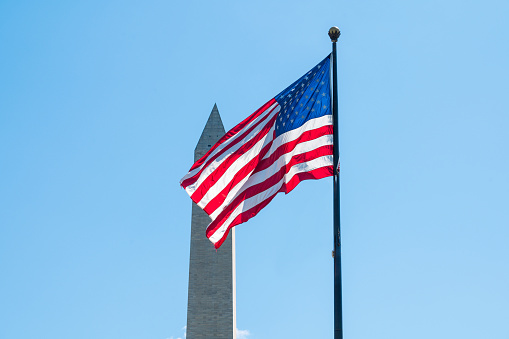 US flag flying from a pole with Washington Monument in background on the National Mall in Washington DC, USA