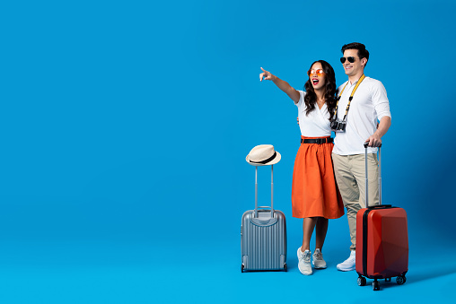 Happy smiling interracial tourist couple with luggage enjoying their summer vacation getaway together in blue studio background