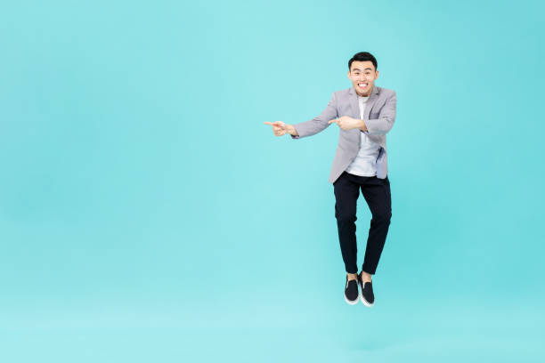 Young smiling Asian man jumping and pointing hands to copy space