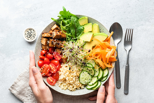 Buddha bowl salad in female hands, balanced meal. Bright grey concrete background, table top view. Weight loss, dieting concept