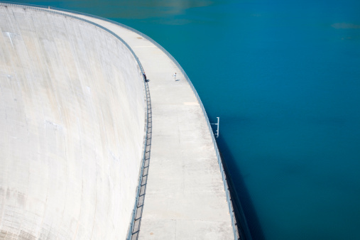 Dam with flowing water at hydroelectric power station at reservoir lake of river. Aerial view