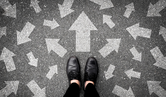 Selfie of feet and arrows on road. Top view. Businessman in black shoes standing floor with many white arrow pathway sign choices. Future life with different direction symbol. Business success concept.