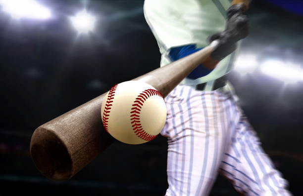 野球選手は、スタジアムのスポットライトの下でクローズアップでバットでボールを打つ - 野球 ストックフォトと画像