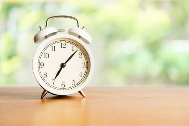 istock White alarm clock on brown wood desk on blurred background with copy space 1176477536